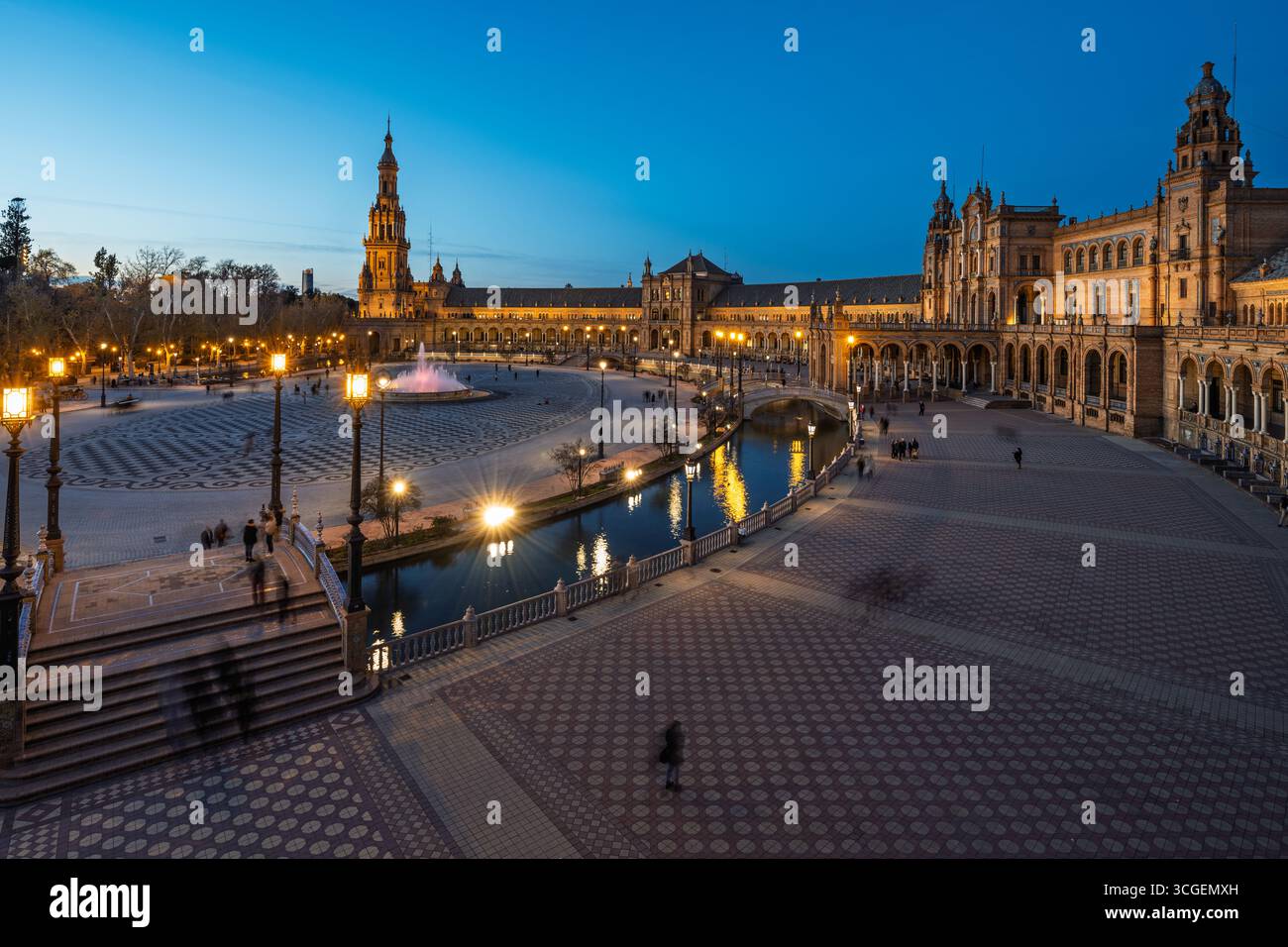 Alors que le crépuscule descend sur Séville, les lumières se reflètent sur l'eau de la Plaza de Espana, créant une atmosphère tranquille pour les promenades en soirée. Banque D'Images