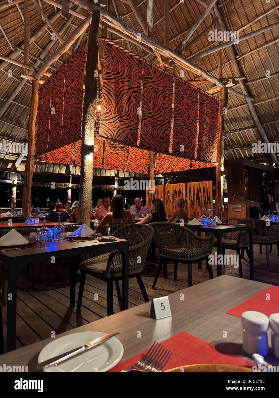 Intérieur de restaurant tropical la nuit à Zanzibar, Tanzanie, avec un design en bois, une atmosphère chaleureuse, et les clients dînant dans un cadre de villégiature relaxant - Image de stock capturée avec un smartphone