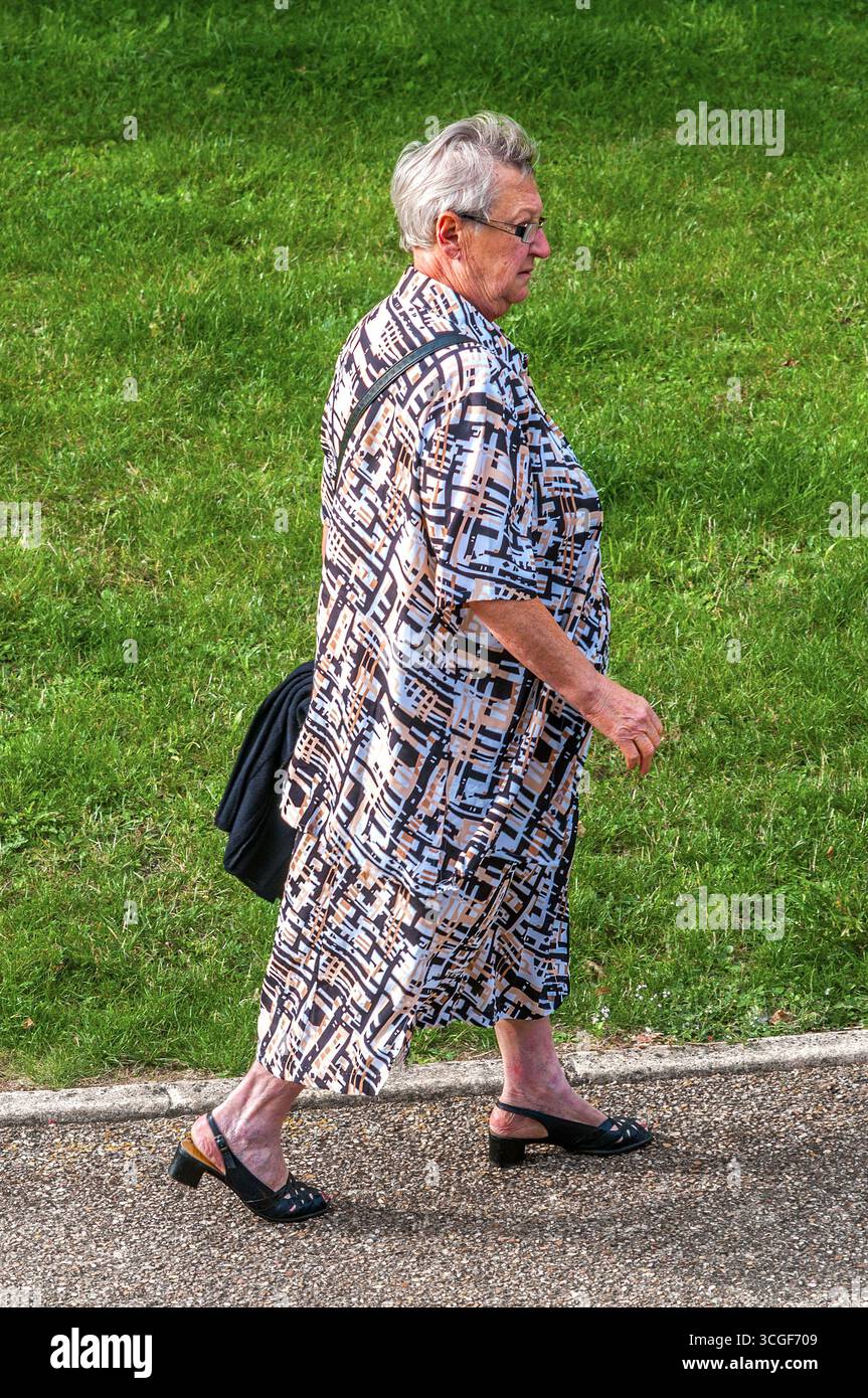 Vue aérienne d'une femme âgée en longue robe abstraite de conception marchant sur le trottoir - Preuilly-sur-Claise, Indre-et-Loire (37), France. Banque D'Images