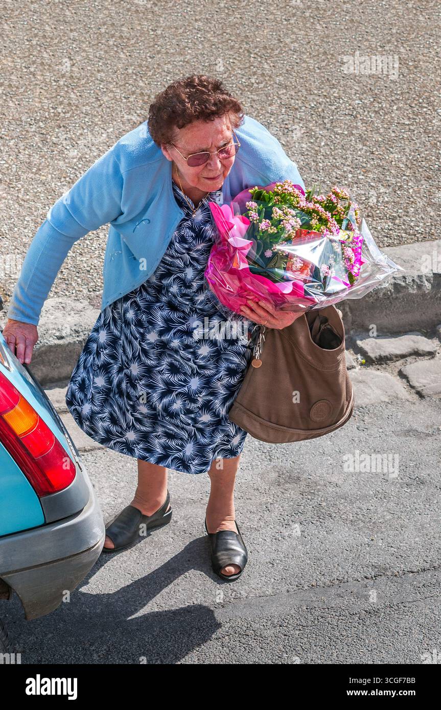 Vue aérienne d'une femme âgée avec un grand bouquet de fleurs traversant la rue derrière la voiture - Preuilly-sur-Claise, Indre-et-Loire (37), France. Banque D'Images