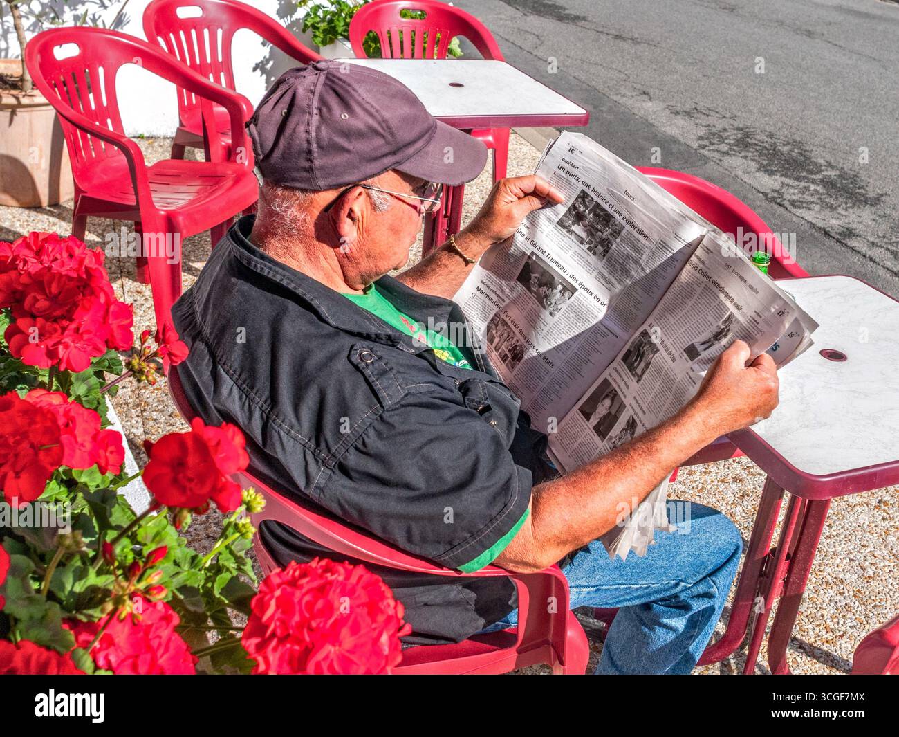 Homme assis à la table du café en plein air lisant un journal local - Preuilly-sur-Claise, Indre-et-Loire (37), France. Banque D'Images
