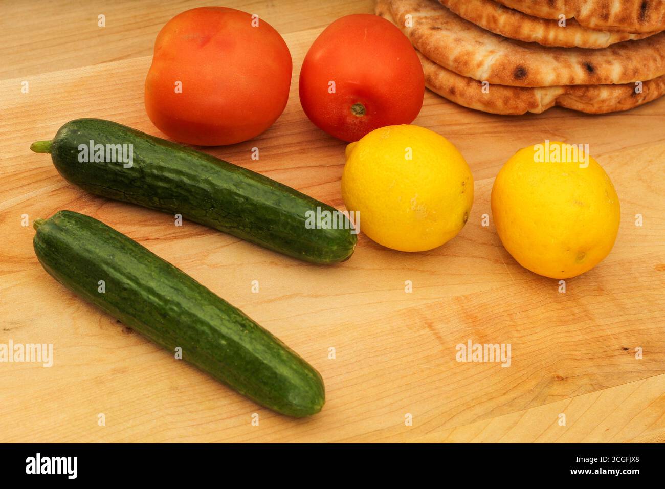 Citrons entiers, concombre et tomate sur planche à découper en bois, affichage coloré Banque D'Images