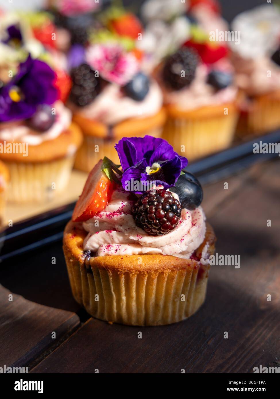 Cupcake aux baies d'été héros par Peggy Porschen avec glaçage aux baies meringue, surmonté de fraise, myrtille, mûre et fleur comestible. Banque D'Images
