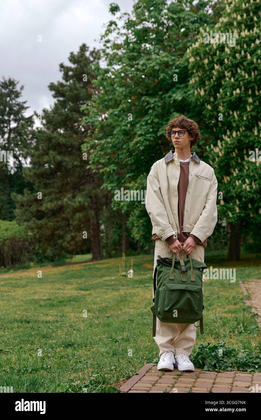 Beau jeune homme se promène dans un parc animé, appréciant l'air frais et les paysages. Banque D'Images