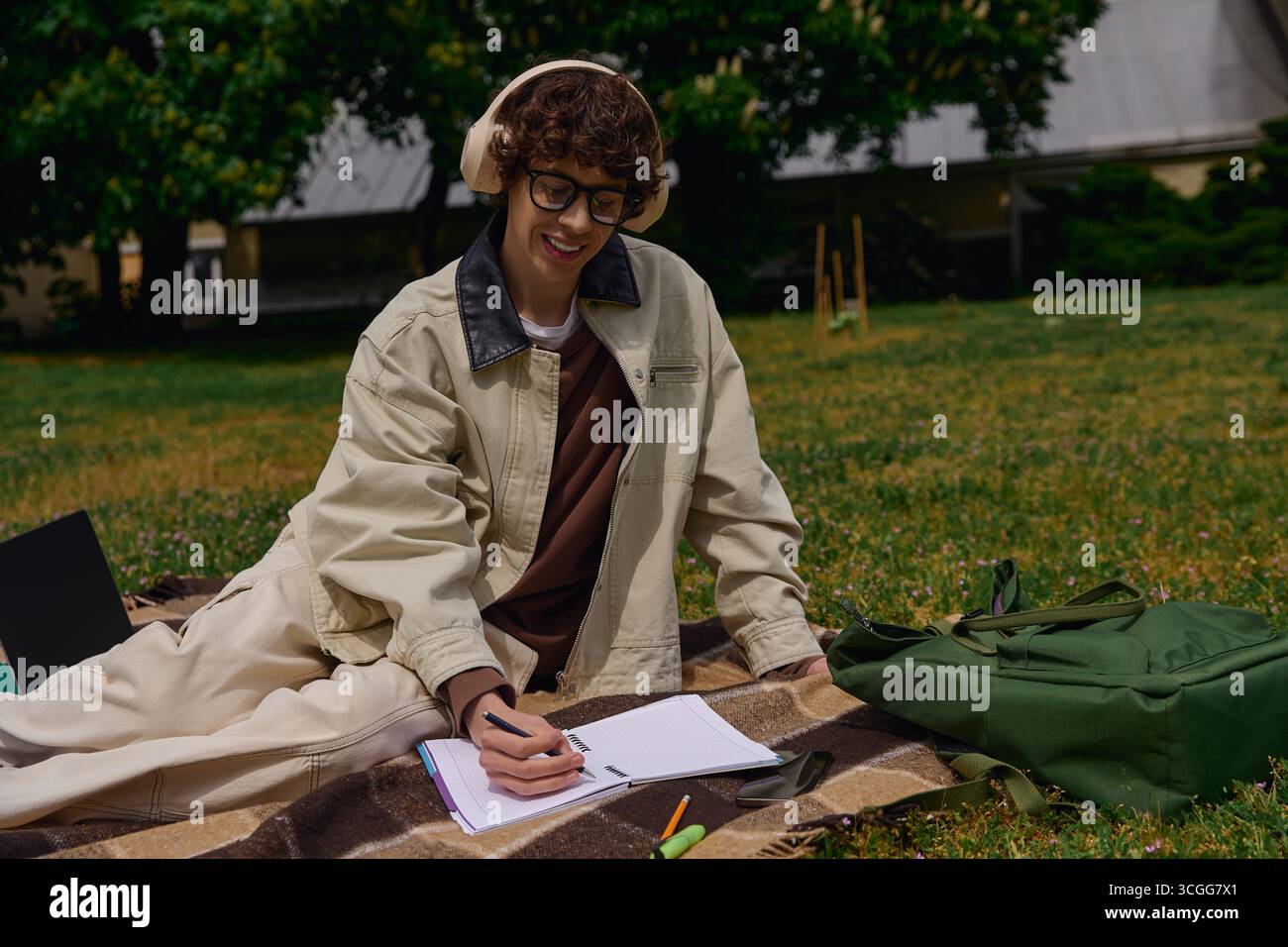 Jeune homme se détend sur une couverture dans le parc, écrivant des notes et profitant du beau temps. Banque D'Images