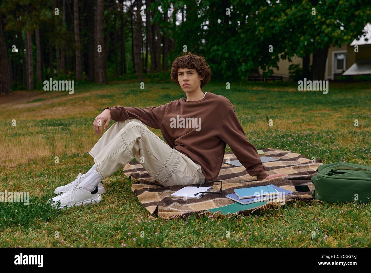 Un jeune homme se détend sur une couverture dans un parc verdoyant tout en profitant de la beauté de la nature. Banque D'Images
