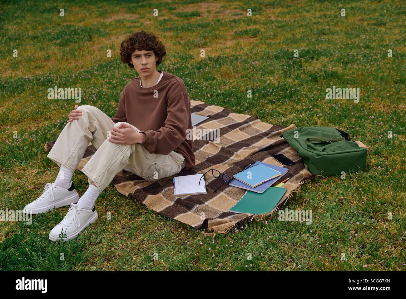 Un jeune homme se détend sur une couverture dans une zone herbeuse, s'engageant dans une réflexion tranquille au milieu de la nature. Banque D'Images