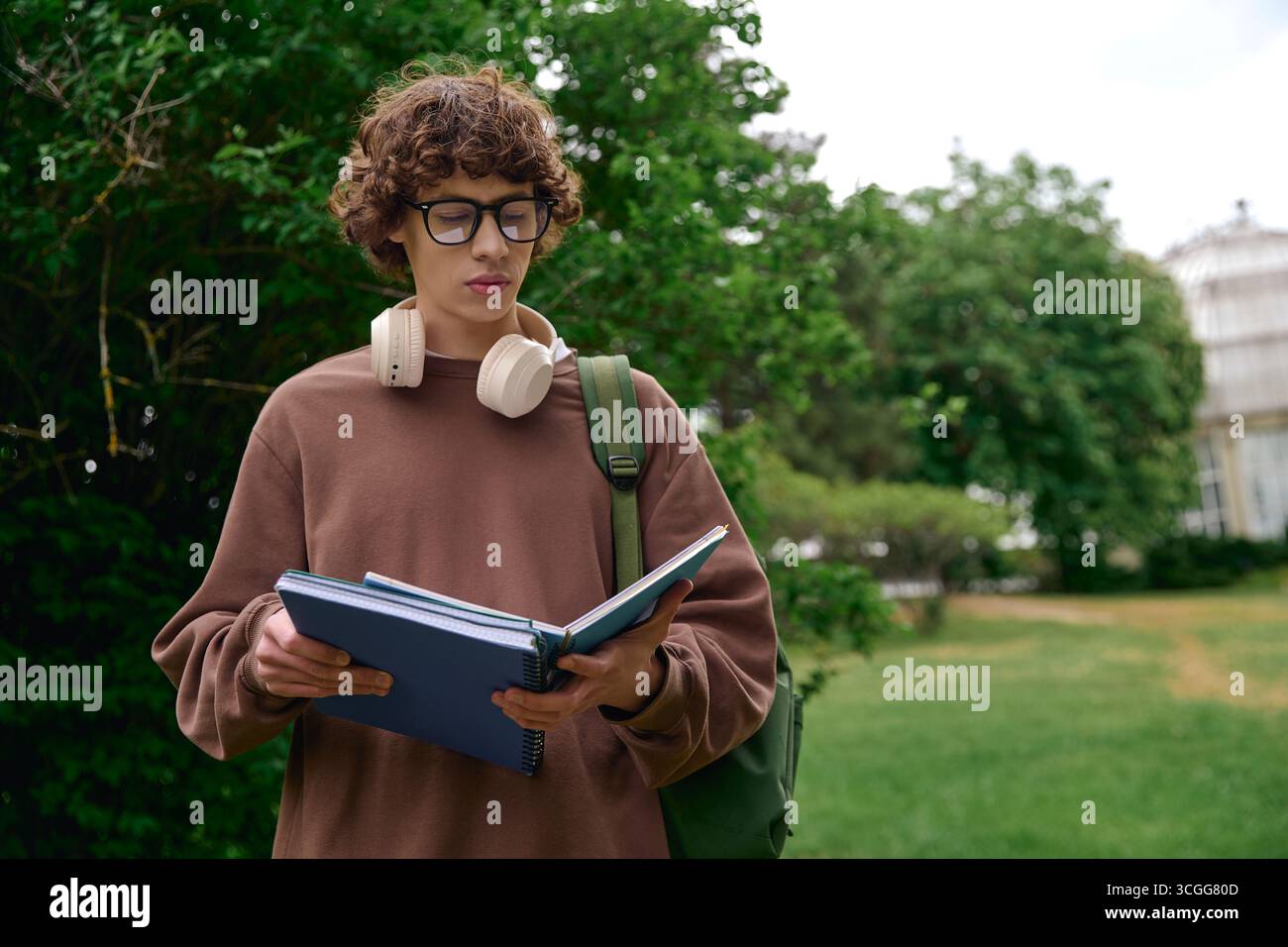 Un jeune bel étudiant aime une promenade paisible à l'extérieur, lisant un livre au milieu de la nature. Banque D'Images