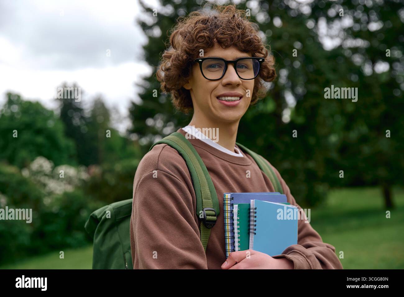 Beau jeune homme prend une promenade dans un cadre paisible en plein air, transportant son matériel d'étude. Banque D'Images