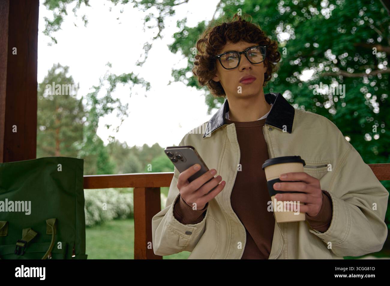 L'étudiant se promène tranquillement à l'extérieur en appréciant la nature avec son café et son téléphone à la main. Banque D'Images