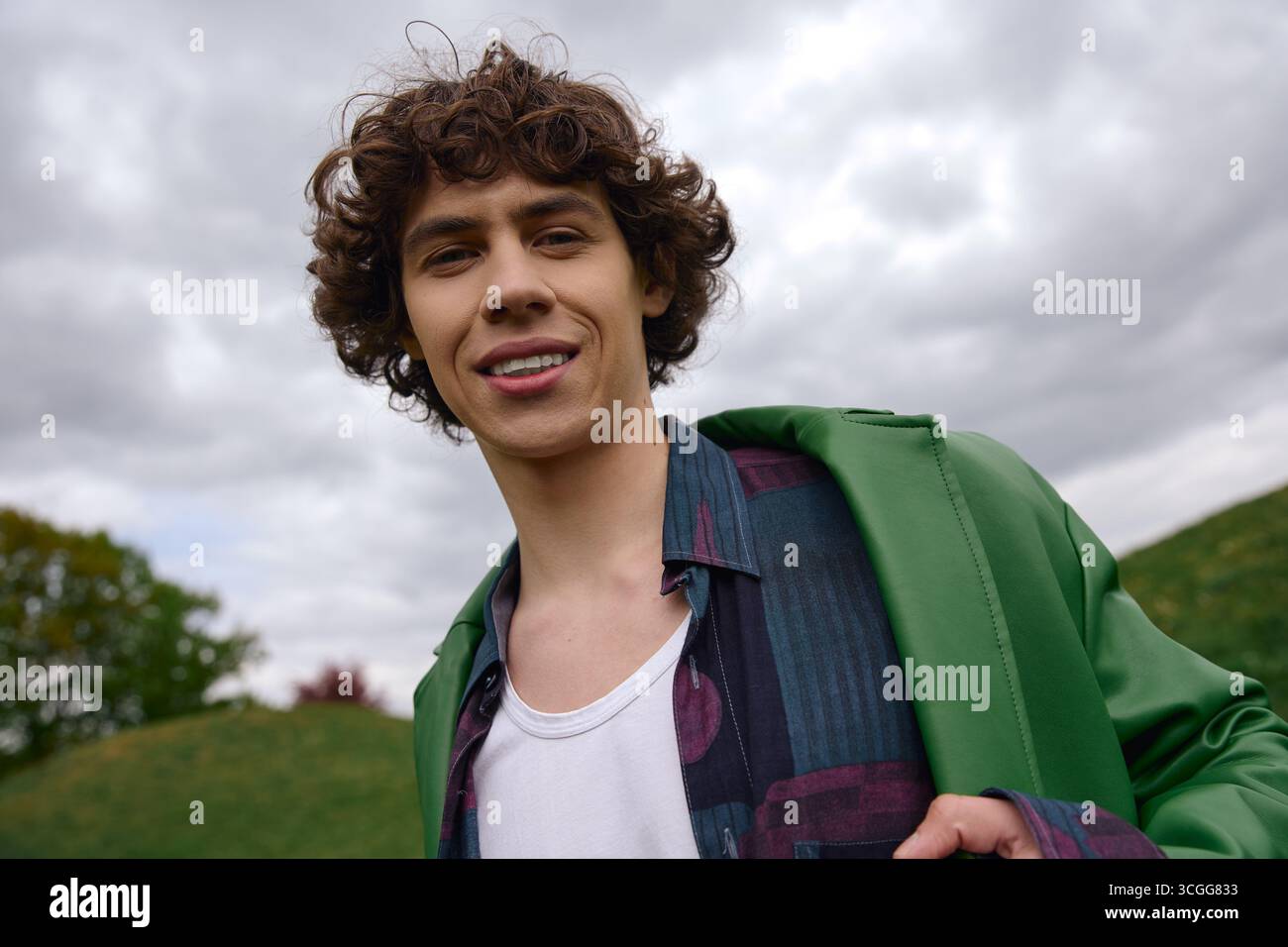 Un étudiant charismatique se promène dans un paysage luxuriant, souriant sous un ciel nuageux. Banque D'Images