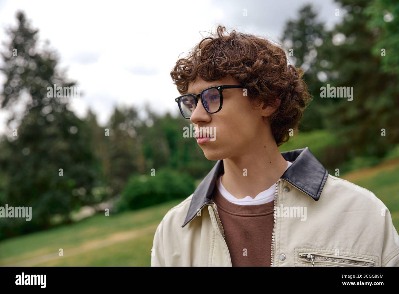 Un beau jeune homme se promène dans un paysage verdoyant, appréciant la sérénité du plein air. Banque D'Images