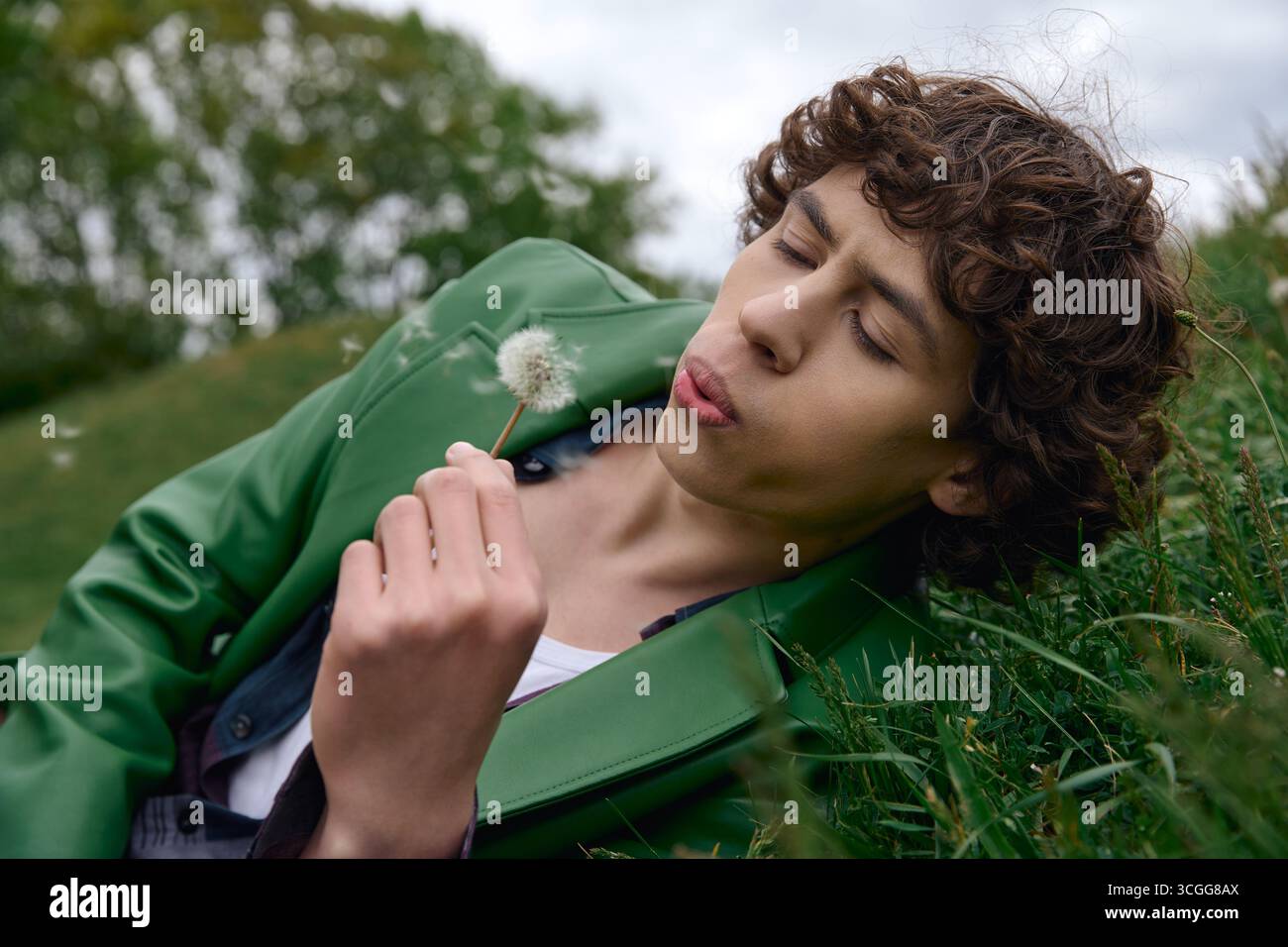 L'élève se détend sur l'herbe, entouré de verdure, soufflant doucement sur une bouffée de pissenlits. Banque D'Images