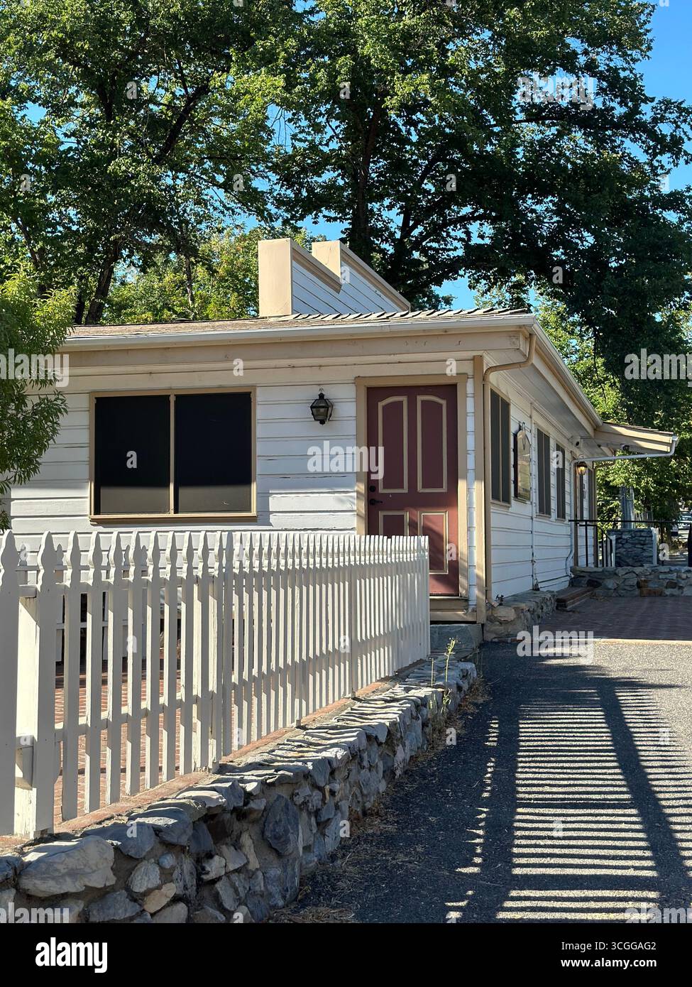 Une maison traditionnelle en bois avec une porte d'entrée rouge et une clôture blanche, entourée d'arbres dans une petite ville californienne. - Image de stock capturée avec un smartphone