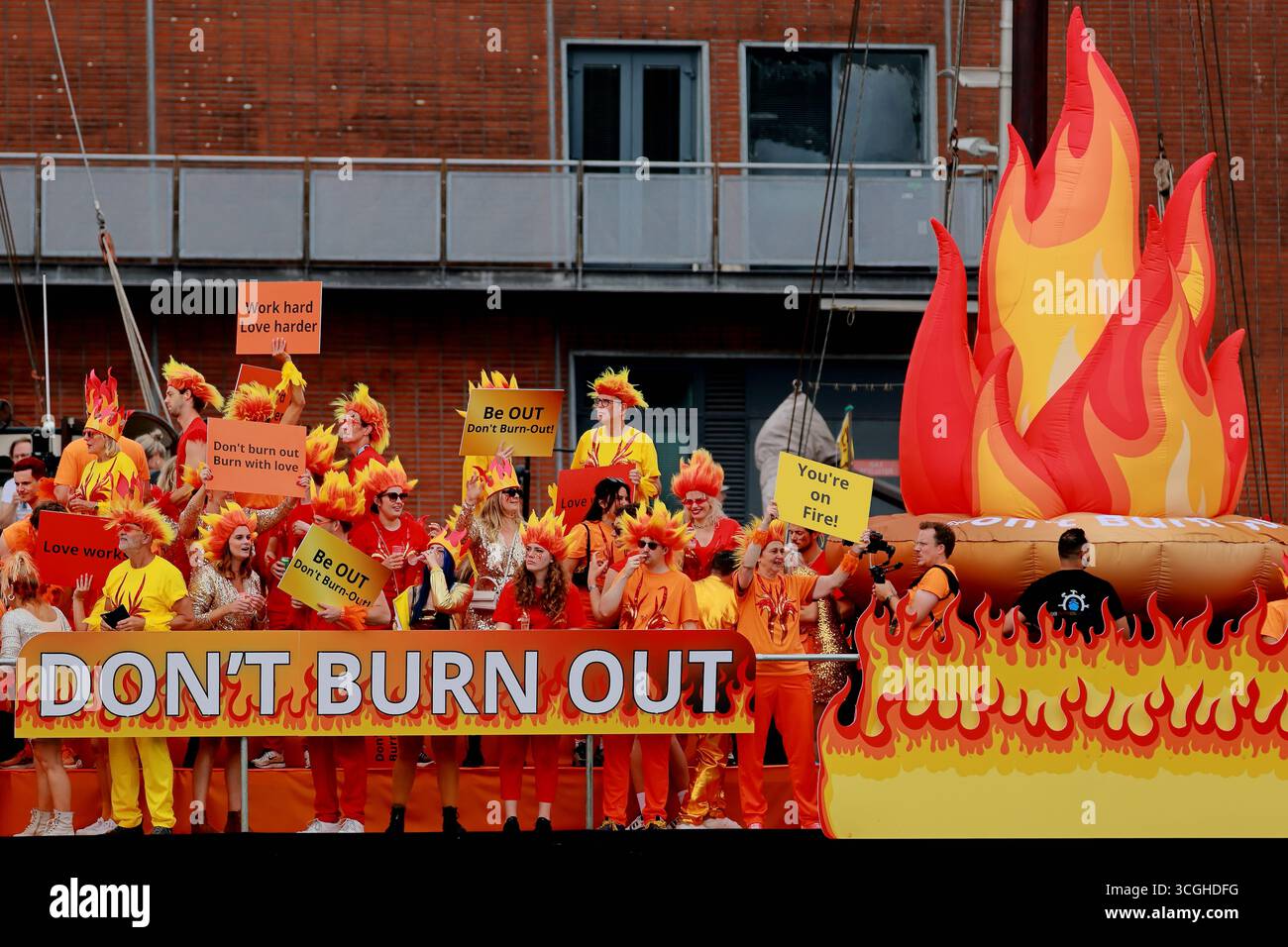 Vue rapprochée des participants en costumes orange tenant des pancartes sur un bateau « ne brûlez pas » à la Pride Amsterdam canal Parade à Amsterdam, pays-Bas. Banque D'Images