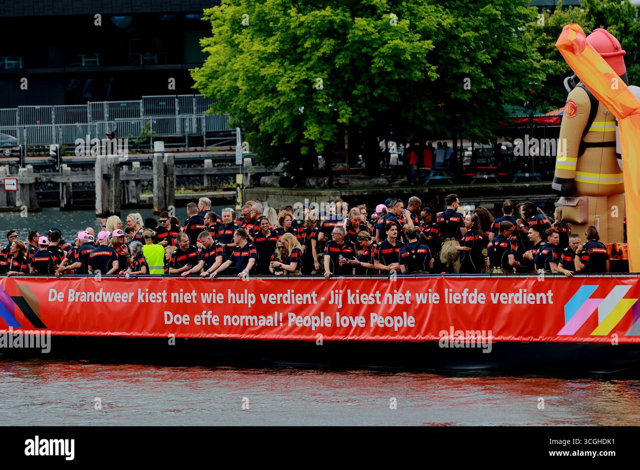 Équipage des pompiers d'Amsterdam sur un bateau de parade du canal Pride avec une bannière et des uniformes néerlandais, se déplaçant le long de l'eau à Amsterdam, au centre-ville des pays-Bas. Banque D'Images