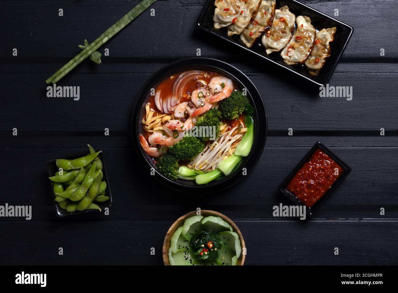 Pose à plat de soupe de nouilles de crevettes avec edamame, boulettes et légumes verts sur la surface sombre. Cuisine asiatique conçue pour la photographie culinaire commerciale. Banque D'Images