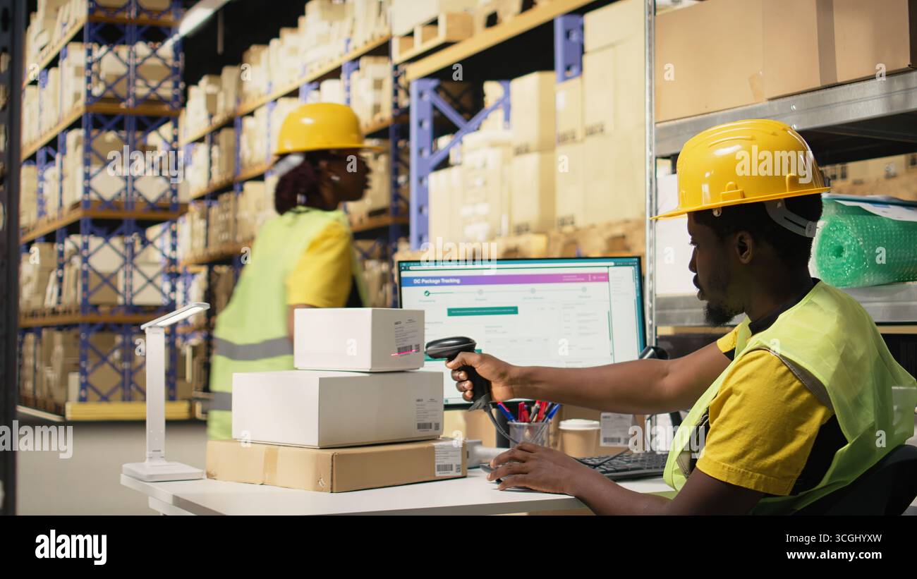 Employé afro-américain fixant les étiquettes et scannant les étiquettes de code-barres sur les boîtes, enregistrant les détails de la marchandise et de l'expédition avant la distribution. Utilisation du scanner pour le suivi des informations. Caméra A. Banque D'Images