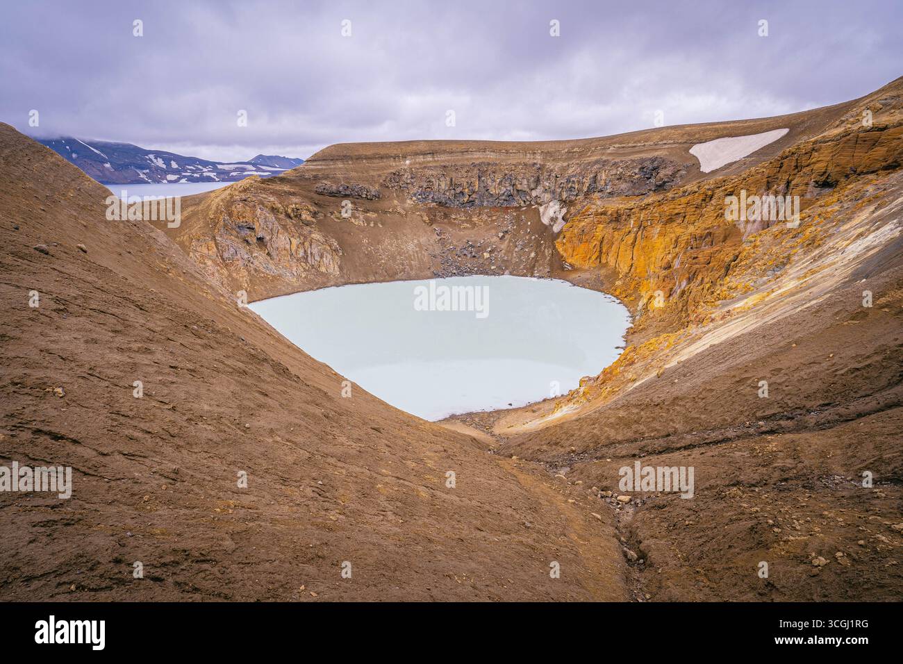 Le cratère Víti dans la caldeira Askja en Islande révèle un lac turquoise pâle entouré de pentes volcaniques abruptes de formations rocheuses dorées et brunes Banque D'Images