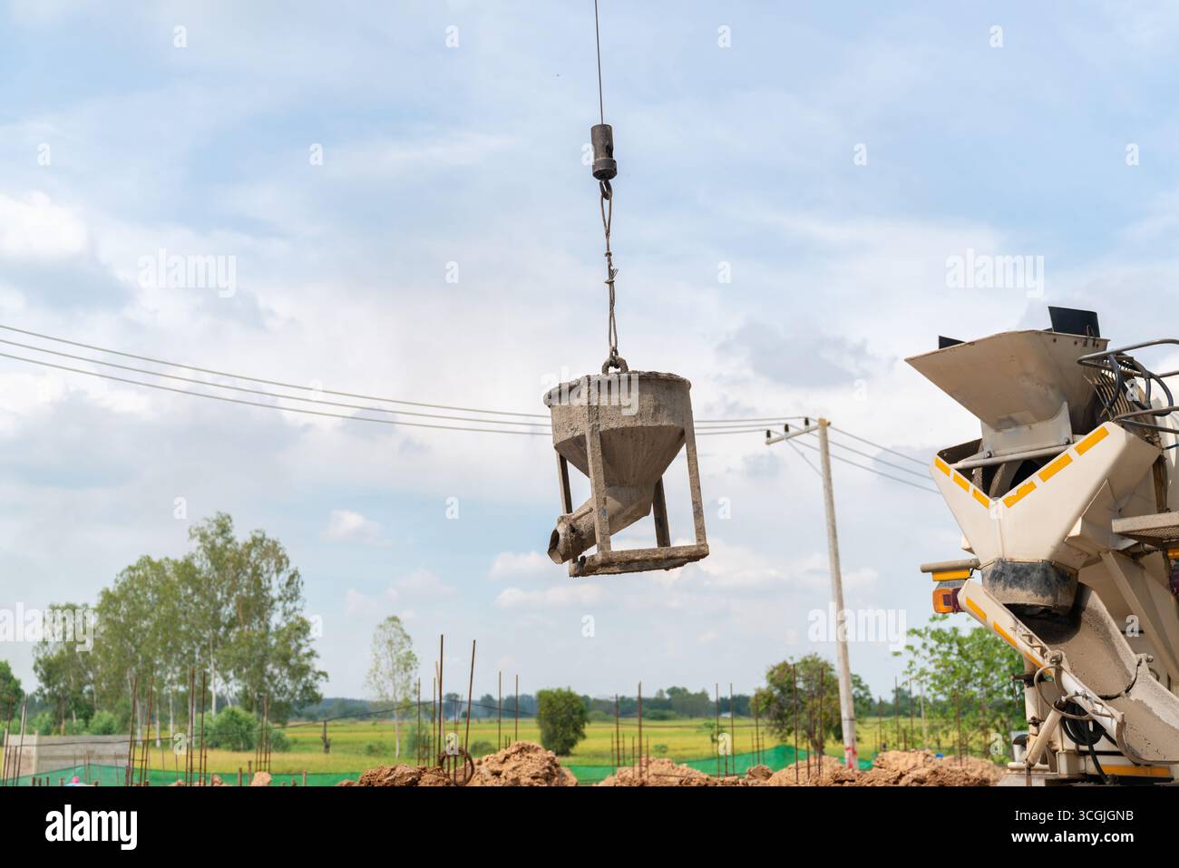 Le seau, utilisé pour couler le béton, est suspendu en plein air dans le cadre d'un processus de construction. A proximité, un camion malaxeur à béton est visible, indiquant Banque D'Images