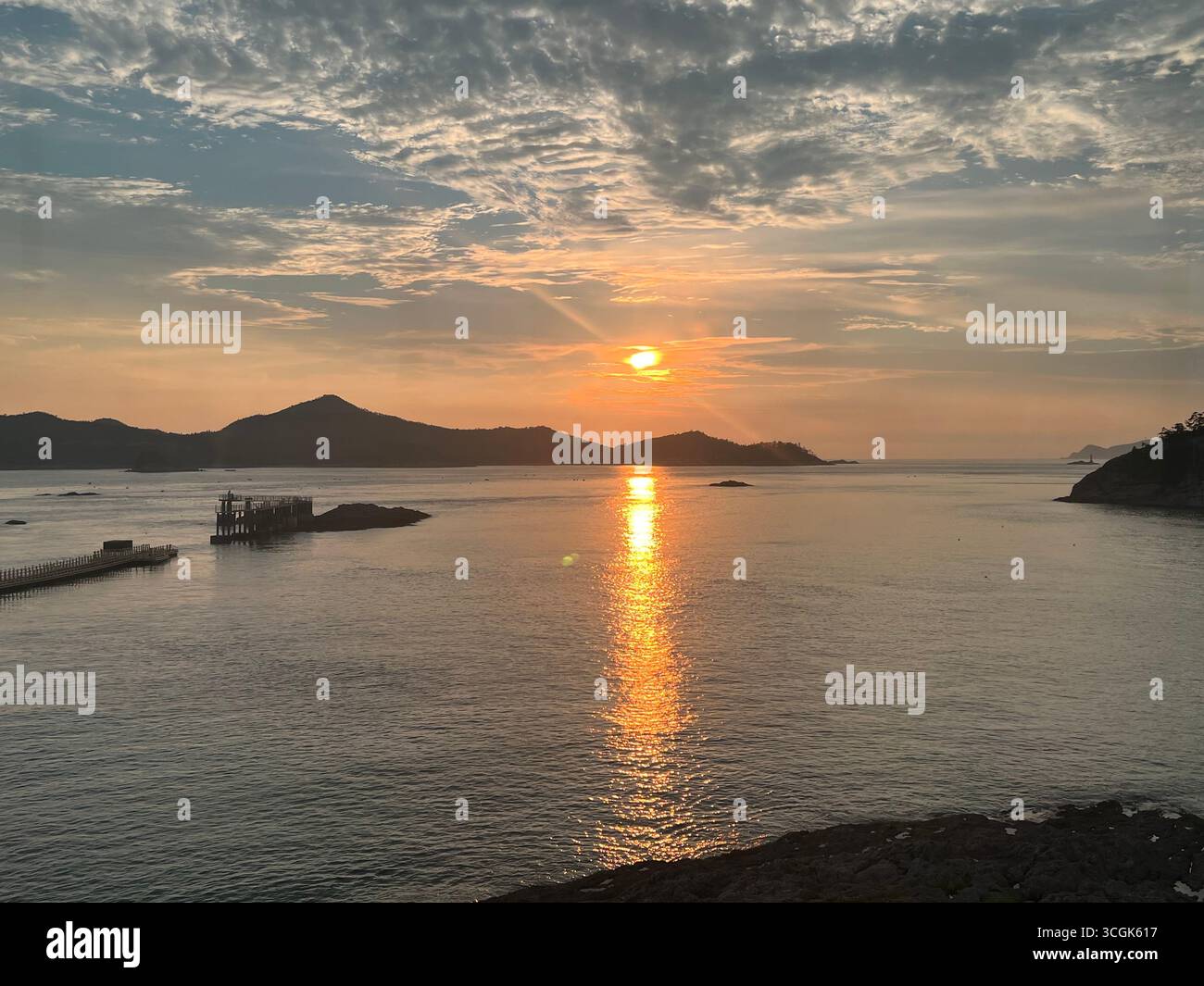 Coucher de soleil sur la mer calme à l'île de Jangjado, Corée du Sud, avec un ciel vibrant reflétant sur les eaux tranquilles et les îles lointaines à l'horizon. - Image de stock capturée avec un smartphone