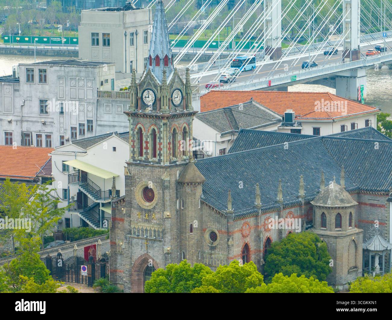 Une vieille église en pierre avec une tour de l'horloge se trouve dans la ville de Ningbo, en Chine. Des bâtiments de la ville, des arbres et un long pont sont vus à proximité. Banque D'Images