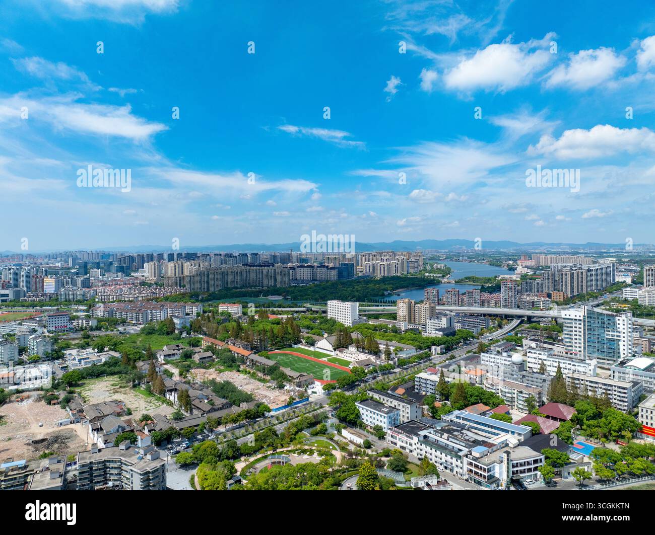La ville de Ningbo, en Chine, offre une vue aérienne panoramique sur ses bâtiments modernes, ses espaces verts et un lac paisible sous un ciel bleu vif. Banque D'Images