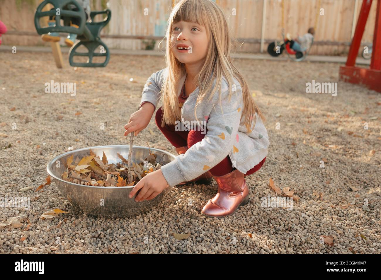 Fille d'âge préscolaire rassemblant des feuilles d'automne sur le terrain de jeu Banque D'Images