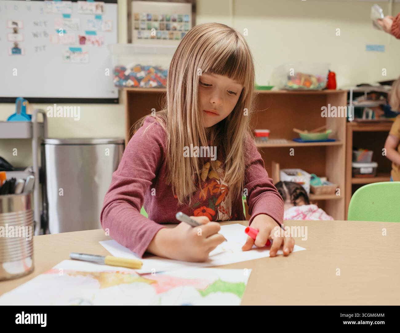 Fille d'âge préscolaire dessinant avec des marqueurs à table dans la salle de classe Banque D'Images