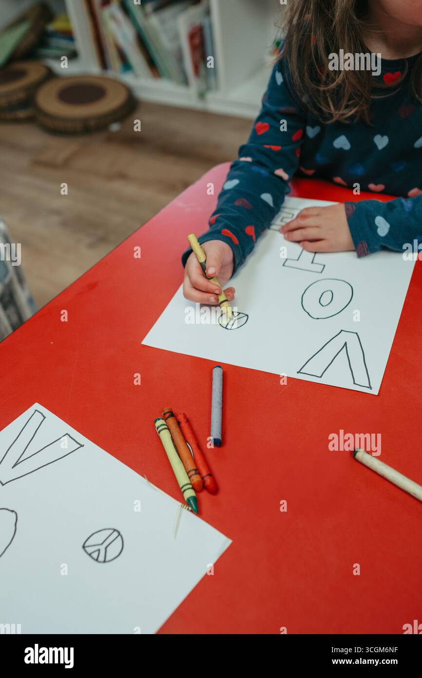 Fille d'âge préscolaire coloriant symbole de paix et le mot vote Banque D'Images