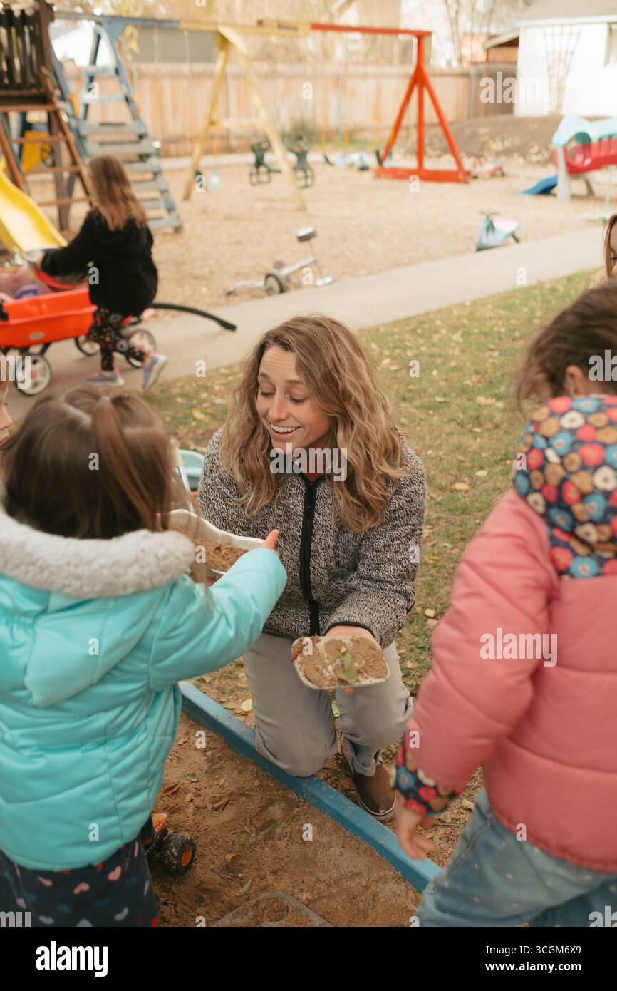 Enseignant s'engageant avec les enfants d'âge préscolaire dans le bac à sable pendant la récréation Banque D'Images