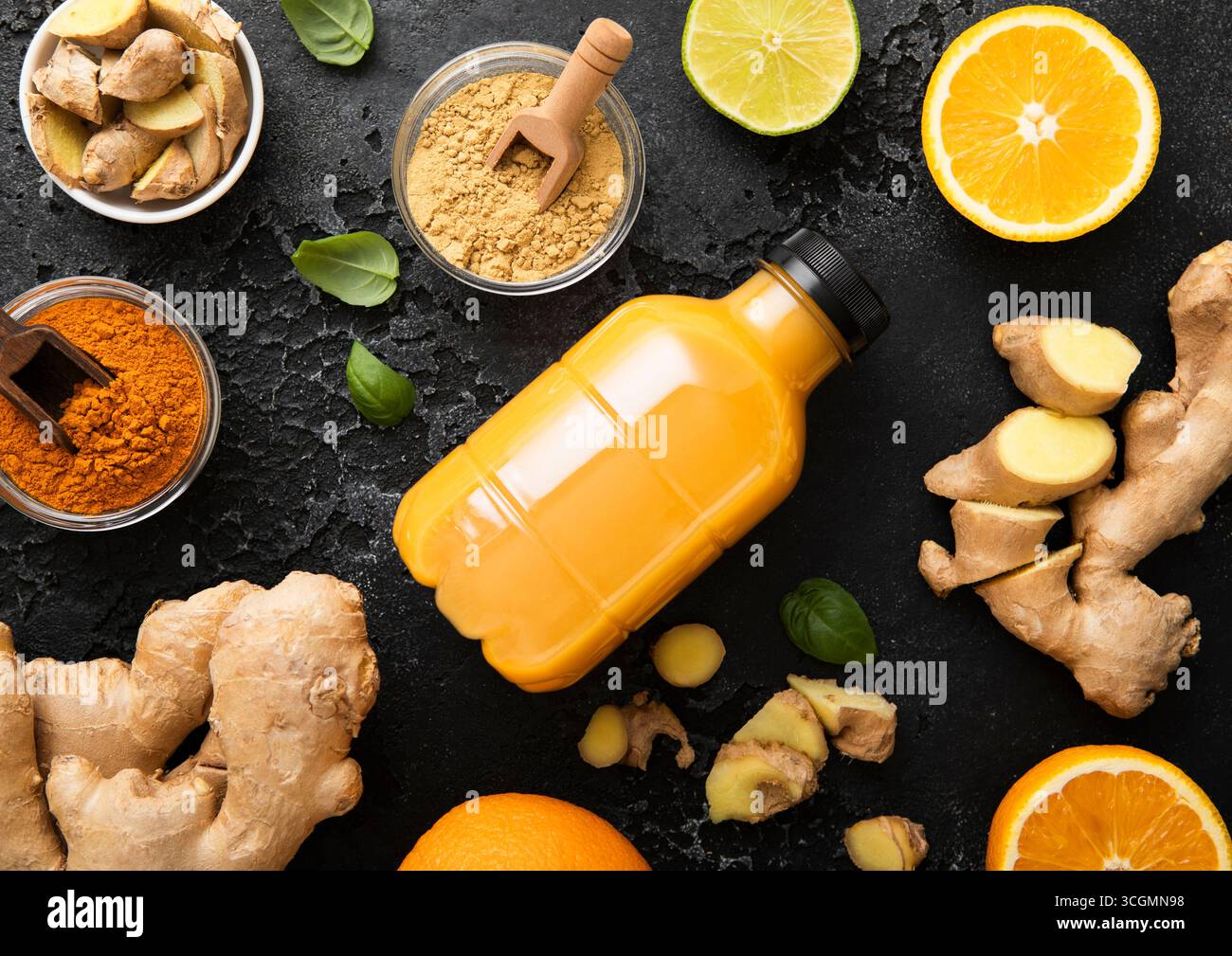 Boisson immunisée au gingembre et à l'orange avec de la racine de gingembre et de la poudre de curcuma sur fond de cuisine noir. Banque D'Images