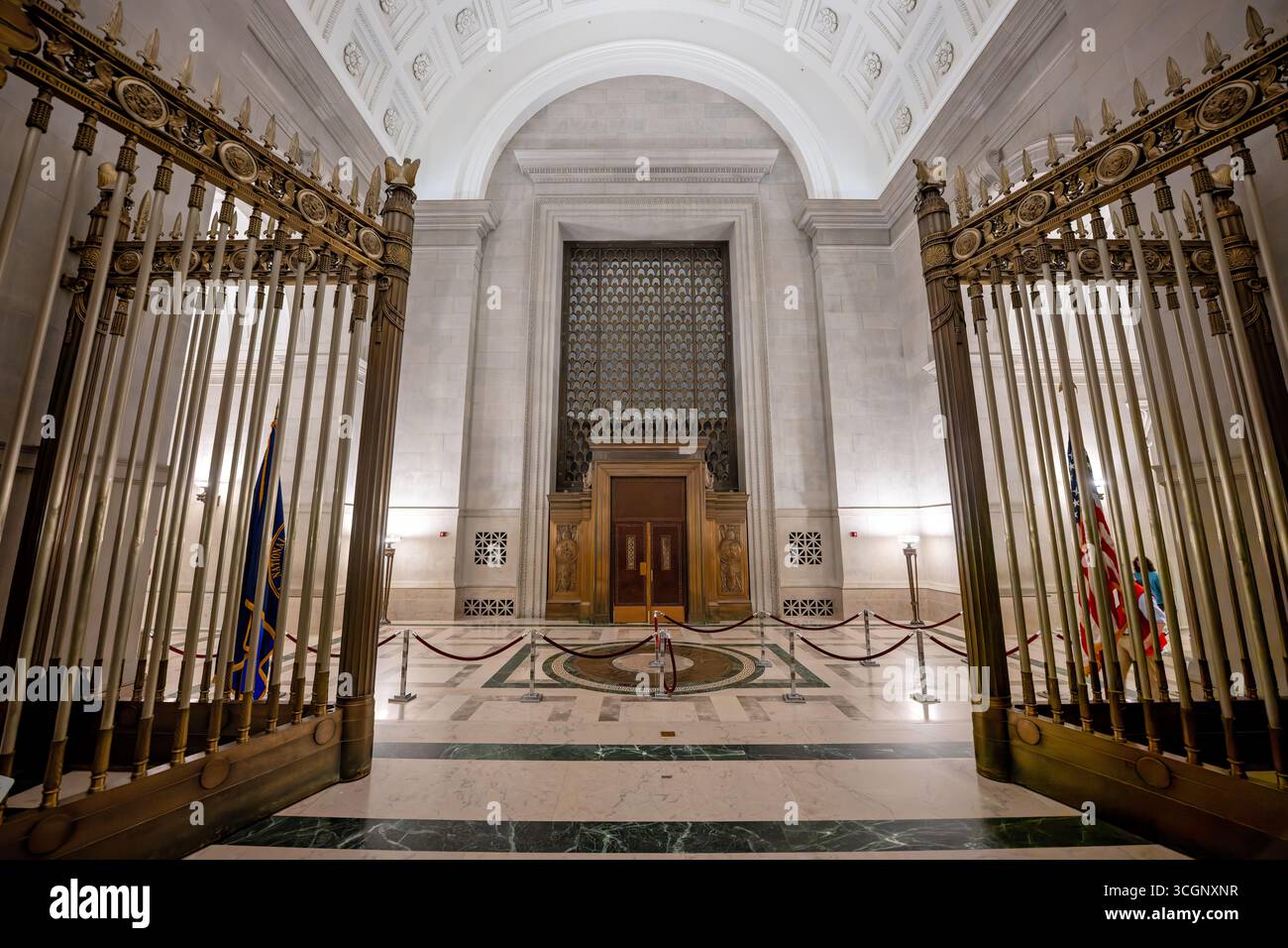 Rotonde des Archives nationales et entrée principale d'origine à Washington DC | WASHINGTON D.C., États-Unis — Des grilles de sécurité en bronze ornées encadrent une vue vers l'entrée principale d'origine du bâtiment des Archives nationales, ses portes lourdes maintenant fermées au public. Conçu par John Russell Pope et ouvert en 1935, ce passage de Constitution Avenue servait autrefois de point d'accès principal avant que les mesures de sécurité ne redirigent le trafic des visiteurs vers d'autres entrées. Banque D'Images