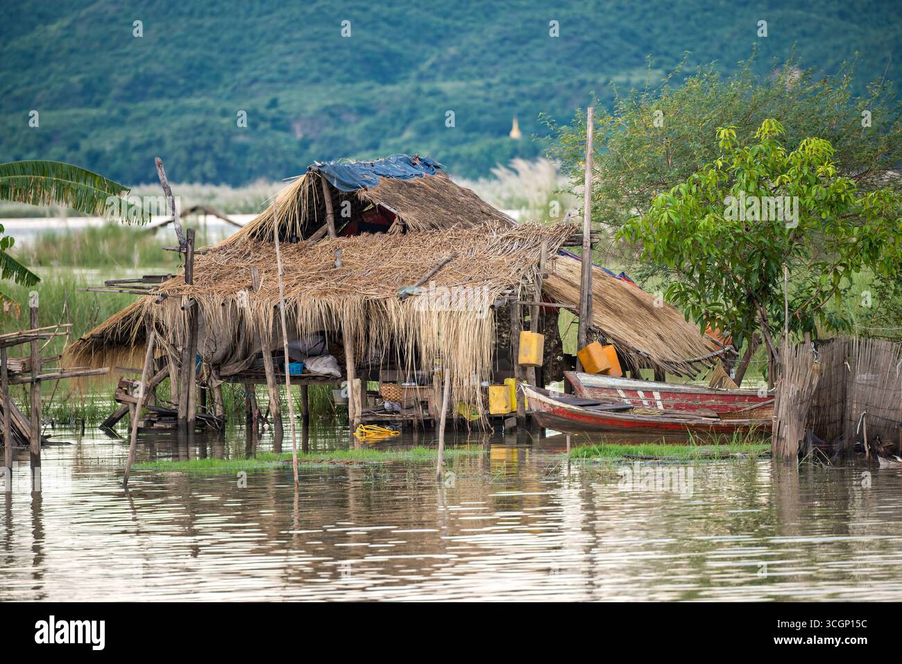 Cabane de pêche au toit de chaume au-dessus de l'eau rivière Ayeyarwaddy Mandalay Myanmar // MANDALAY, Myanmar — Une cabane de pêche traditionnelle au toit de chaume est construite au-dessus de l'eau, une vue commune le long de la rivière Ayeyarwaddy (également connue sous le nom d'Irrawaddy). Ces habitations servent de maisons et de bases aux communautés de pêcheurs locales, s'adaptant aux fluctuations des niveaux d'eau de la rivière. Ils font partie intégrante du paysage riverain et du mode de vie traditionnel dans la région de Mandalay au Myanmar. Banque D'Images