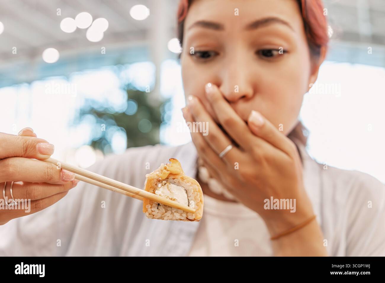 La jeune femme tient un rouleau de sushi avec des baguettes et couvre sa bouche, exprimant le dégoût Banque D'Images