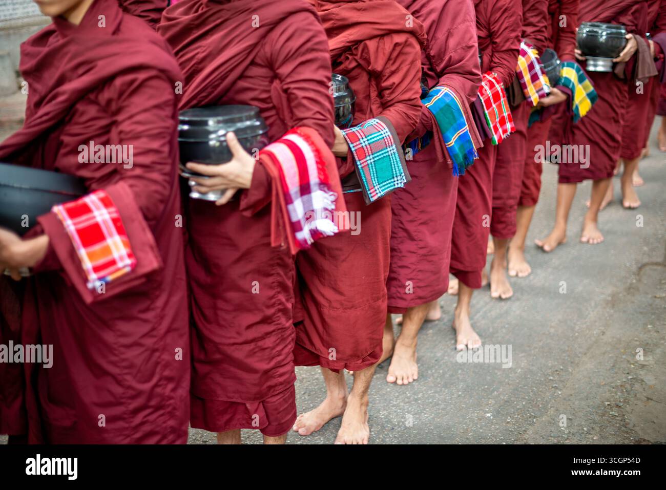 Mahagandayon Monastère novices Alms Bowls Line up Mandalay Myanmar // MANDALAY, Myanmar — les novices bouddhistes pieds nus, connus sous le nom de samaneras, vêtus de robes marron traditionnelles, s'alignent avec leurs bols Alms avant le déjeuner au monastère Mahagandayon. Cette aumône quotidienne, ou pindapata, est une pratique fondamentale dans le bouddhisme Theravada, où les moines et les novices recueillent des offrandes de nourriture de la communauté laïque. Le monastère de Mahagandayon (également connu sous le nom de monastère de Mahagandayone) est l'un des collèges monastiques les plus grands et les plus vénérés du Myanmar. C'est un centre important pour l'éducation monastique et l'studie bouddhiste Banque D'Images
