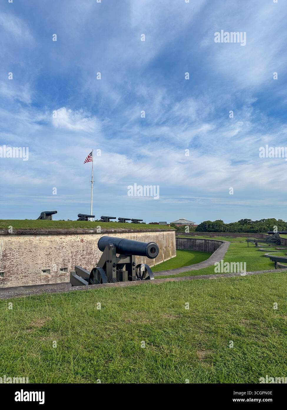 Rangée de canons historiques positionnés le long des remparts herbeux du Fort Macon State Park en Caroline du Nord, avec le drapeau américain flottant fièrement au-dessus. Banque D'Images