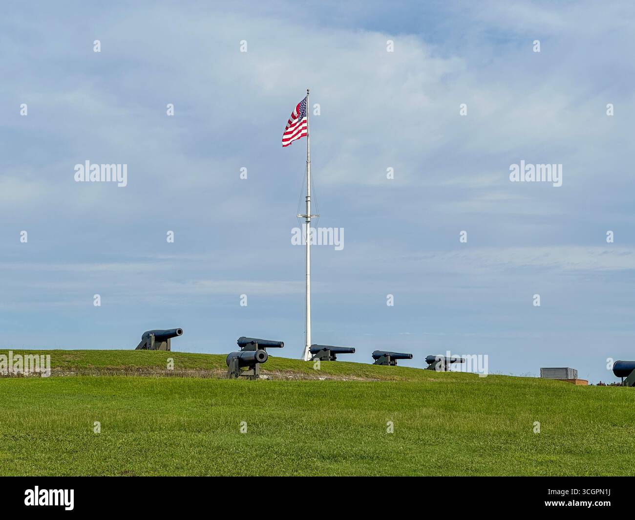 Rangée de canons historiques positionnés le long des remparts herbeux du Fort Macon State Park en Caroline du Nord, avec le drapeau américain flottant fièrement au-dessus. Banque D'Images