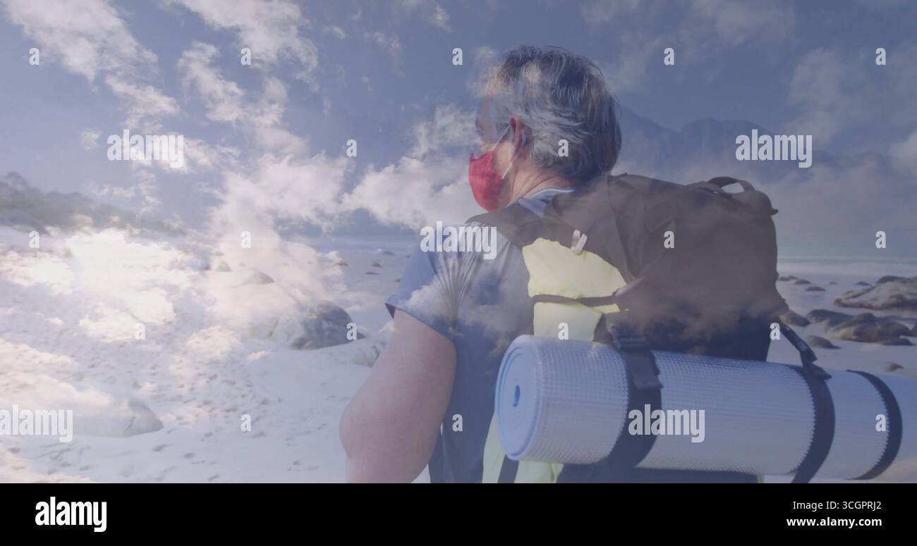 Randonneur debout portant un masque facial rouge sur plaine enneigée, avec sac à dos, tapis, mousqueton, espace copie Banque D'Images