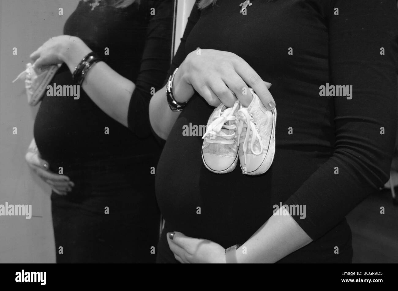 Deux sœurs qui attendent un bébé, l’une enceinte et l’autre avec un enfant, accompagnées d’accessoires de grossesse. Banque D'Images