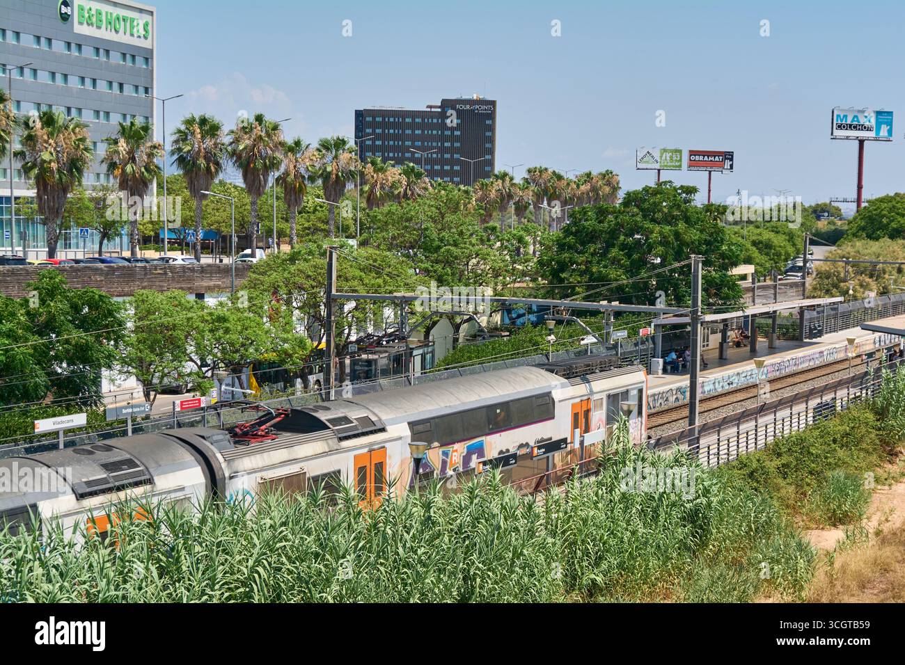 Viladecans. Barcelone - 29 août 2025 : un train Rodalies de Catalunya avec graffitis entre dans la gare de Viladecans, dans un paysage urbain avec des hôtels Banque D'Images