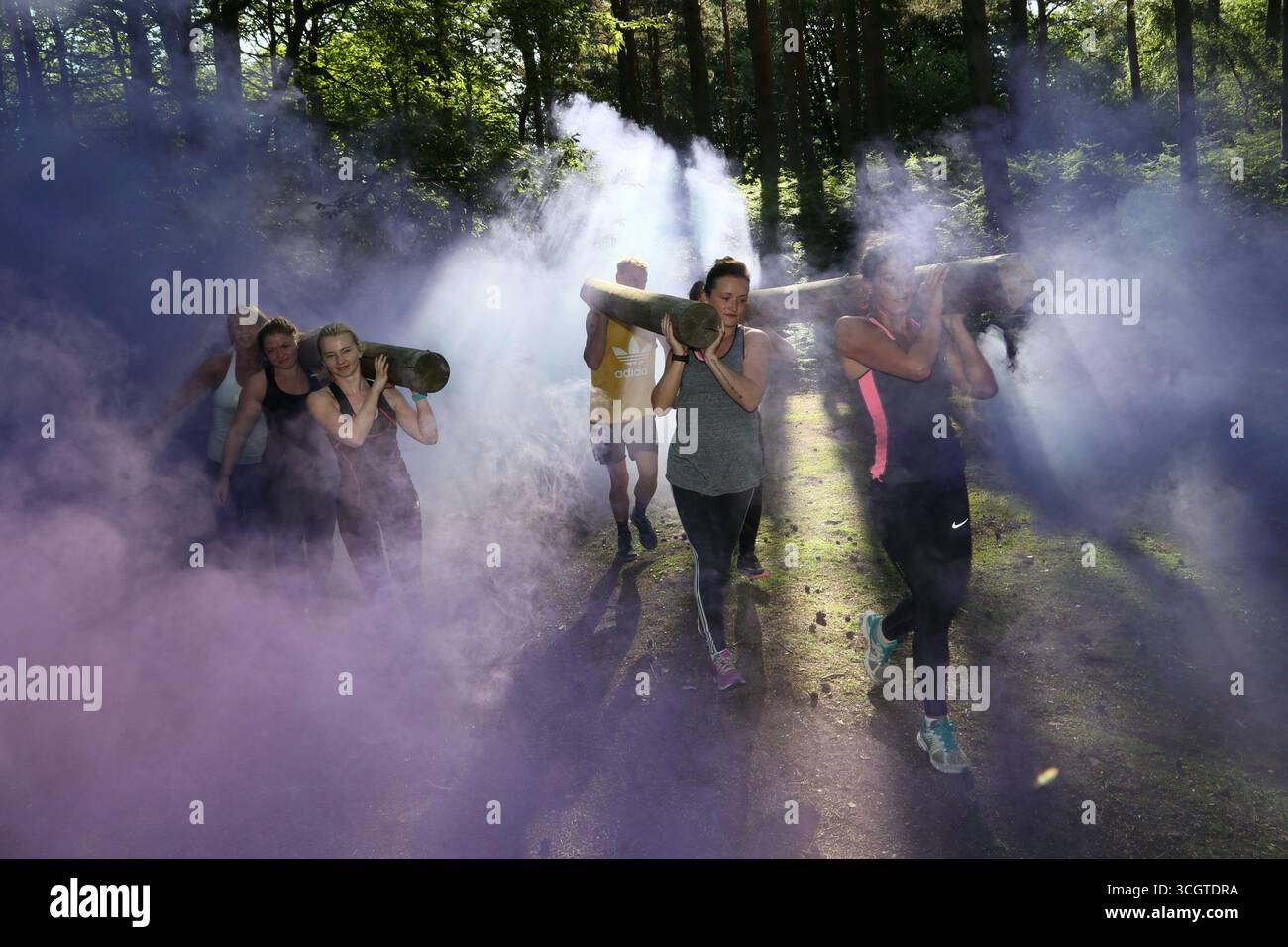 Un groupe de personnes engagées dans une activité physique consistant à transporter de lourdes bûches à travers des nuages de violet fumé dans un bois Banque D'Images