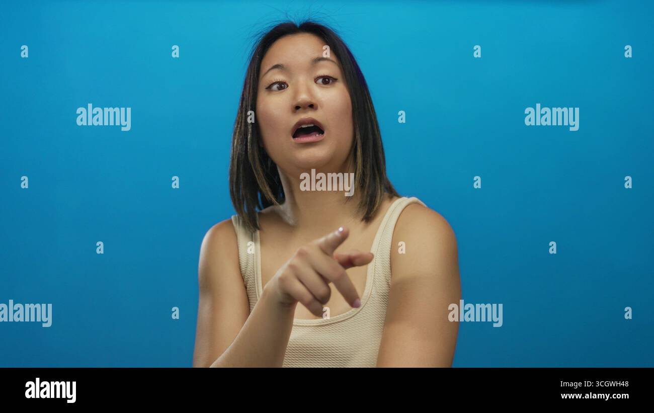 Femme réfléchissant contre un mur bleu solide, s'exprimant avec des gestes de la main, capture un moment de contemplation profonde et de curiosité sous un studio lumineux Banque D'Images