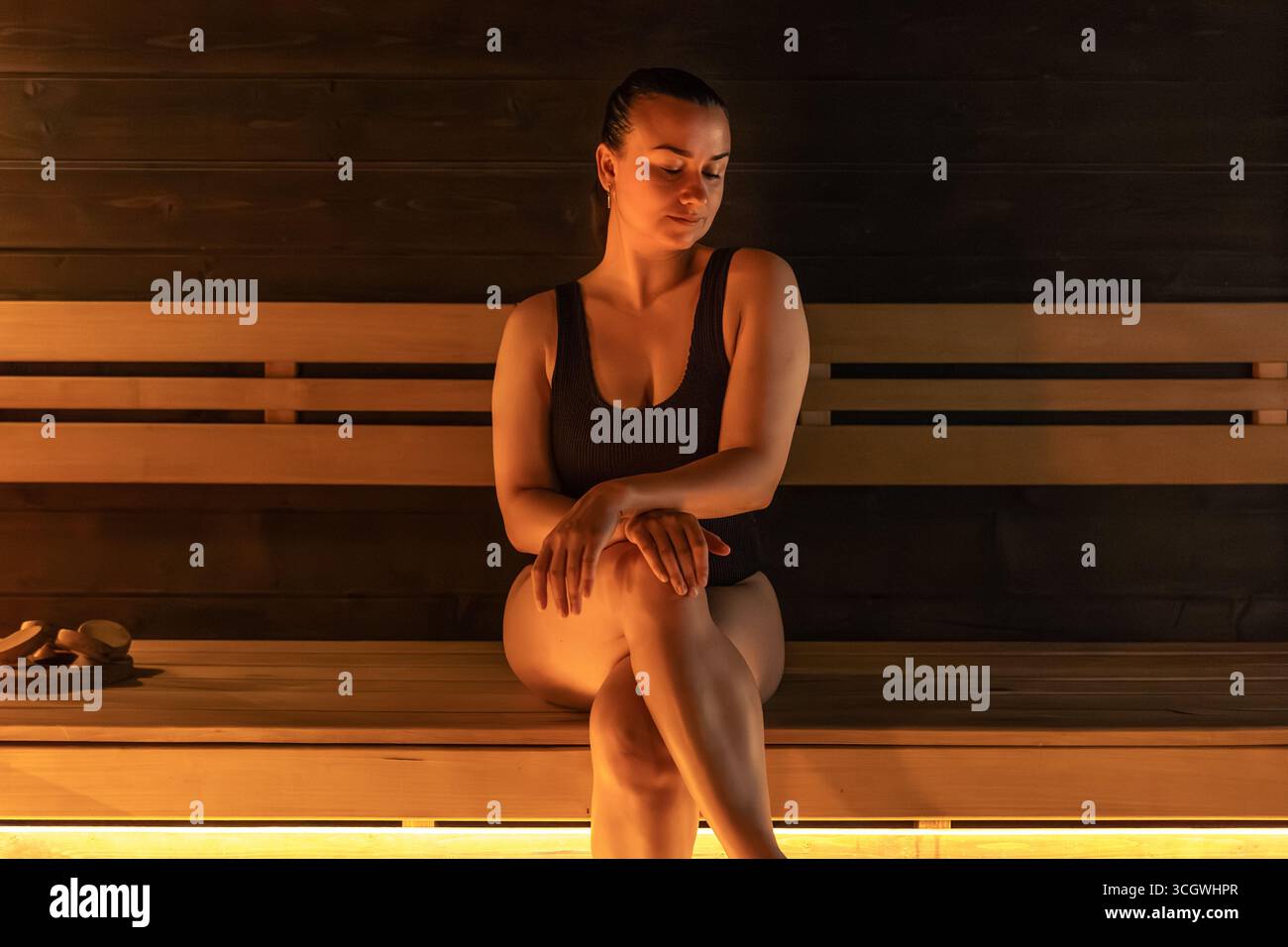 Femme assise sur un banc de sauna, ambiance chaleureuse calme, lumière chaude. Détendez-vous dans le hammam. Banque D'Images