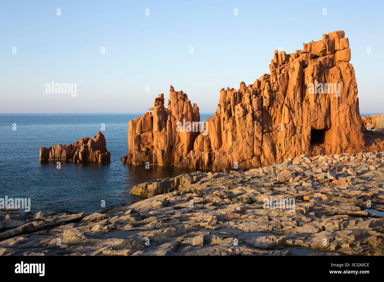 Arbatax, Tortolì, Ogliastra, Sardaigne, Italie. Falaises de porphyre rouge surplombant le rivage rocheux de la Baia delle Rocce Rosse, coucher de soleil. Banque D'Images