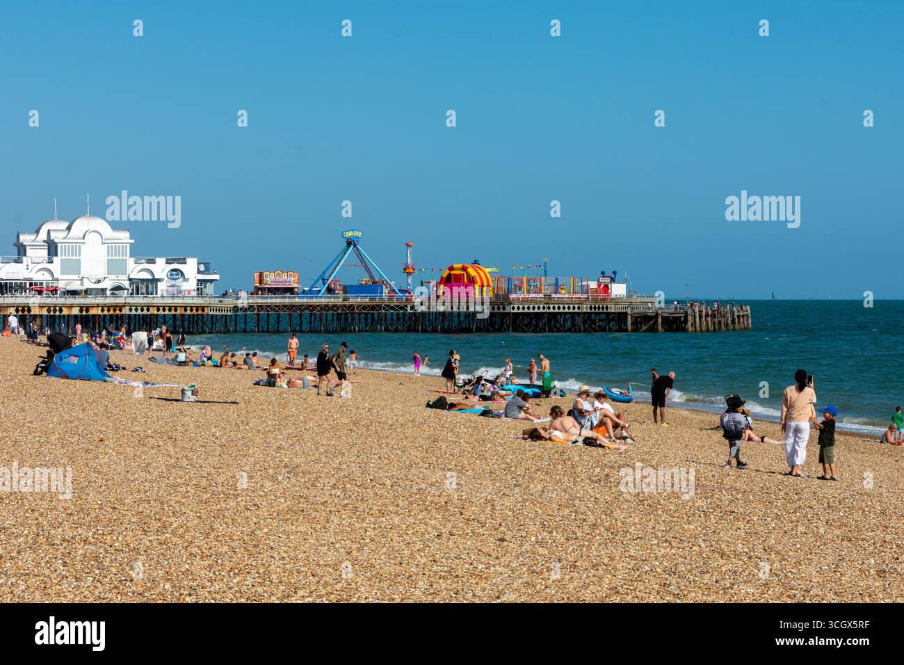 Southsea Beach, Portsmouth, Royaume-Uni - 17 août 2025 : les gens bronzent sur la plage de galets à côté de South Parade Pier, un bâtiment classé Grade II. Banque D'Images