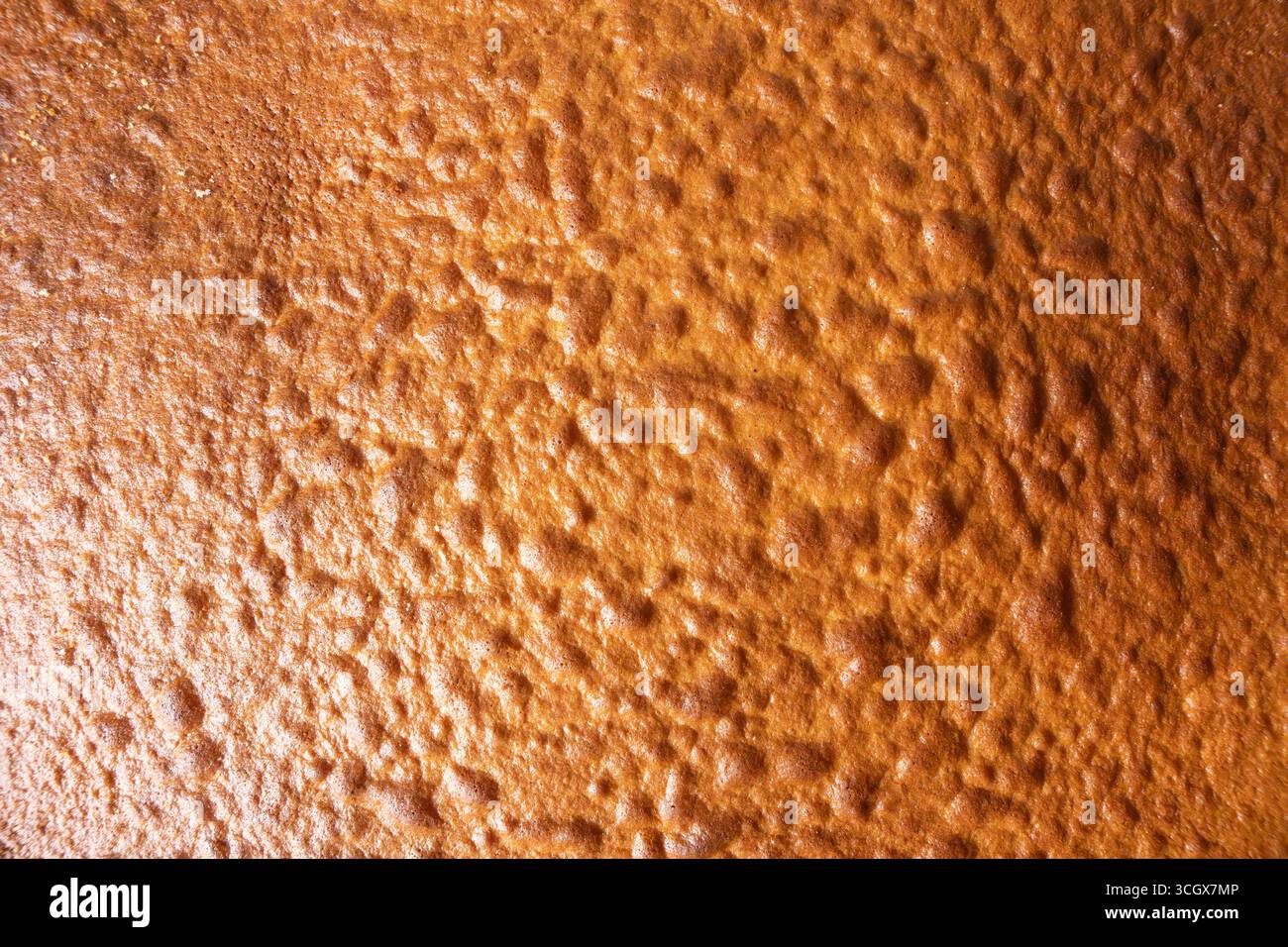 Gros plan d'une surface de gâteau cuit au four brun doré. La texture est aérée, inégale et légèrement brillante. Banque D'Images