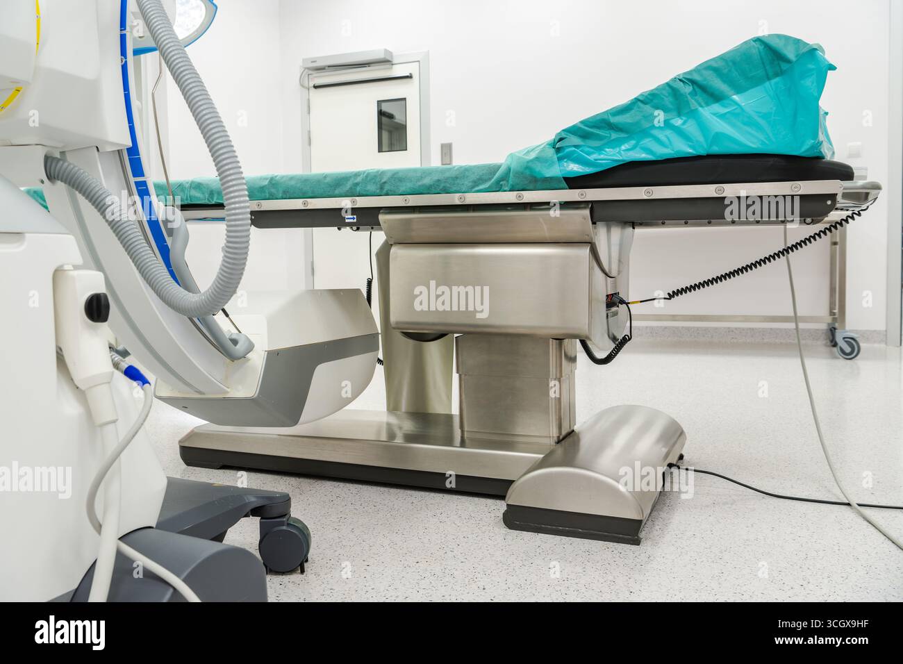 Une salle d'opération d'hôpital organisée dispose d'une table d'examen propre, d'équipements médicaux et d'un éclairage lumineux typique d'un environnement chirurgical. Banque D'Images