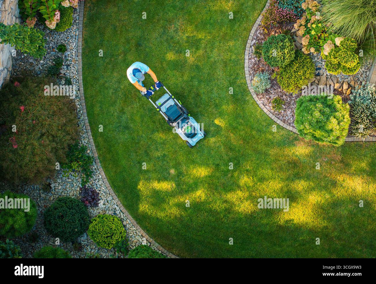 Une personne tond une pelouse verte luxuriante dans un jardin magnifiquement aménagé avec des parterres de fleurs et des plantes décoratives pendant la lumière du jour. Banque D'Images