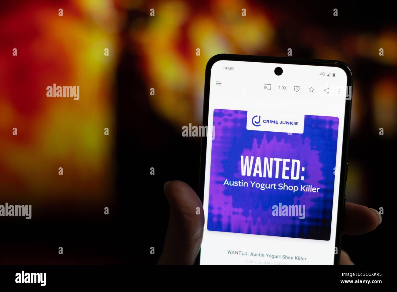 Crime Junkie podcast voulait Austin Yogurt Shop Killer jouant sur un téléphone portable avec un bâtiment en feu en arrière-plan. Banque D'Images